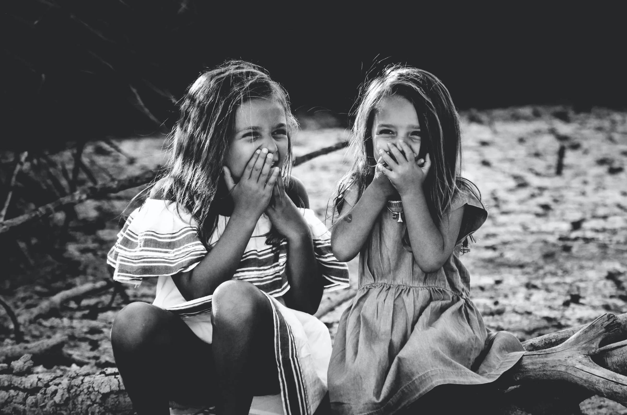 A black and white photo of two little girls as best friends giggling with hands over their mouths.