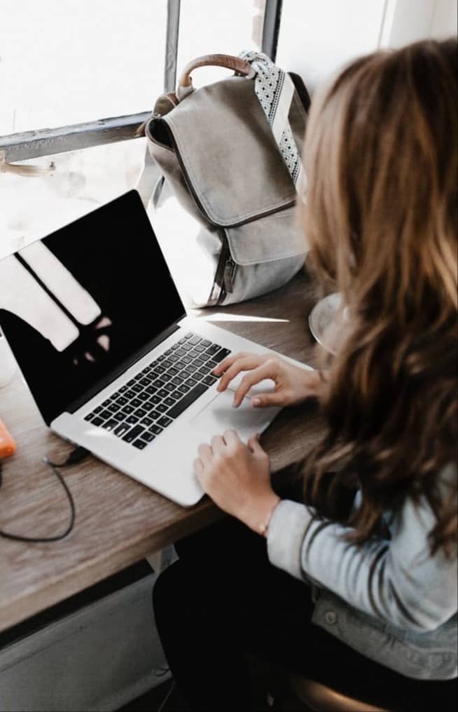 girl wearing grey long-sleeved shirt using MacBook Pro on brown wooden table