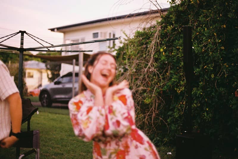 A young woman in a floral dress laughing outdoors.