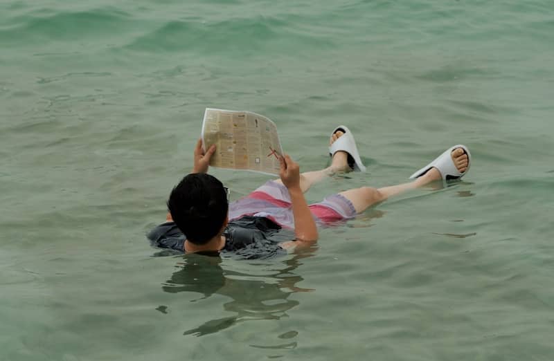 Person floats in calm water reading a newspaper.