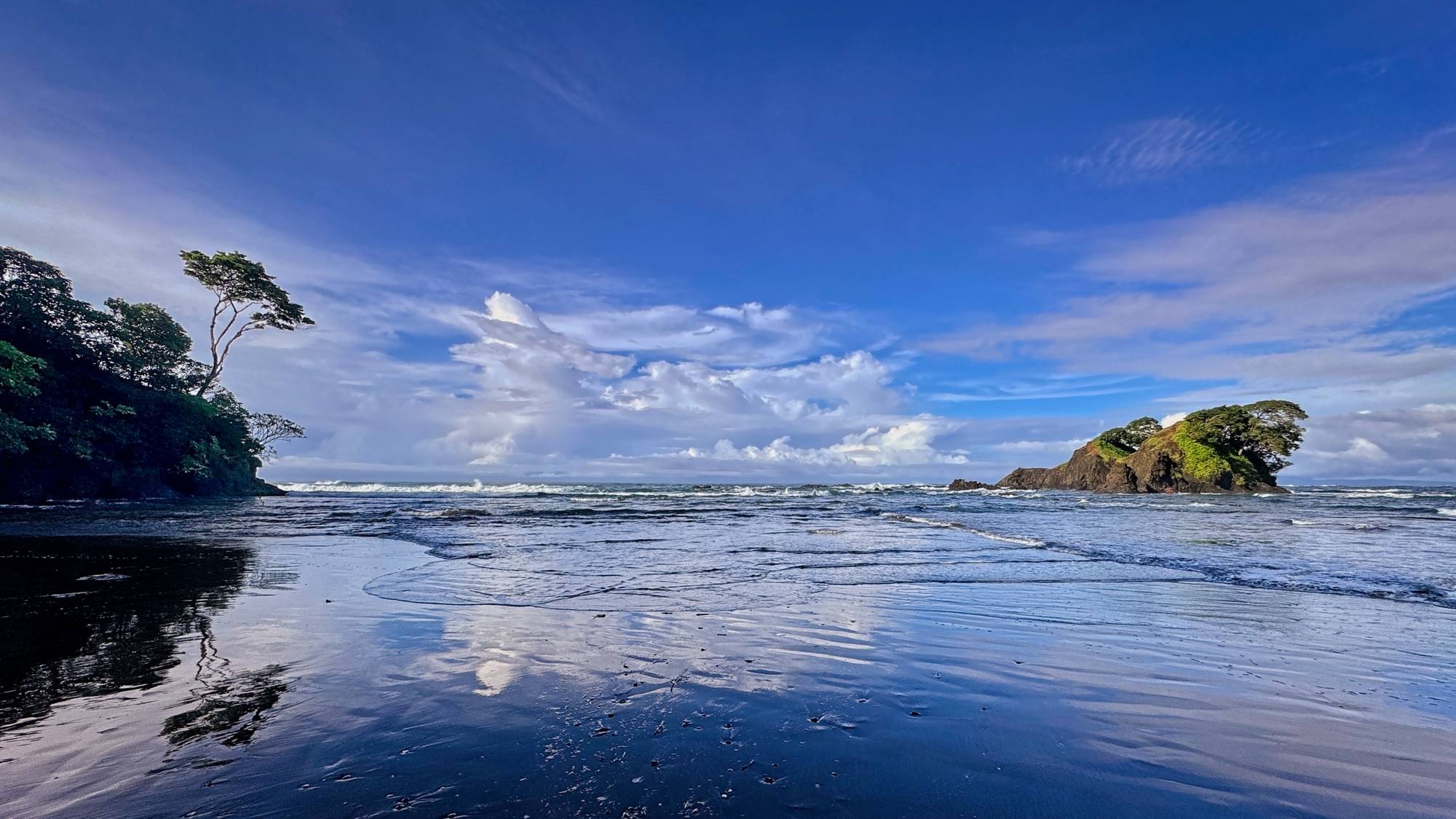 Sunlit beach with clouds reflected into the wet sand. 