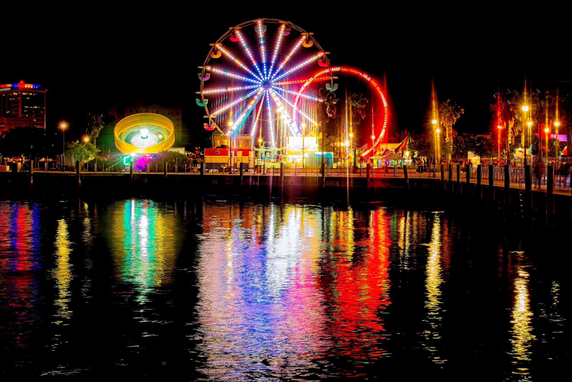 Night view of a oceanside carnival with the ferris wheel reflected in the water. 
