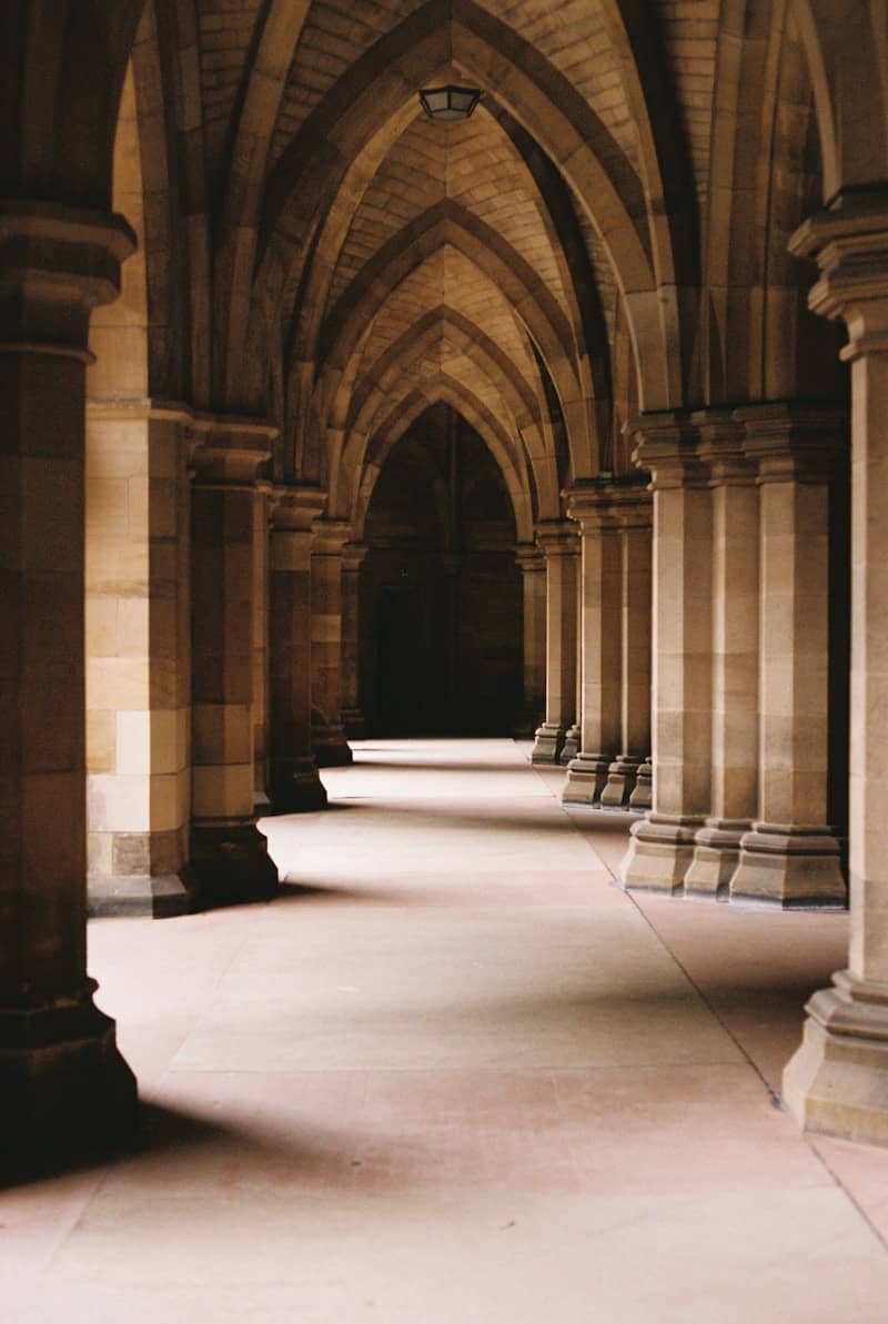 A stone corridor with vaulted ceilings and pillars in a historic building on a college campus. 