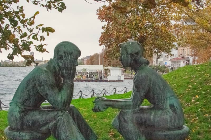 Two bronze statues of people sitting by water