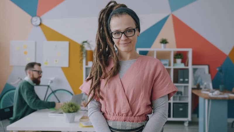 A woman with dreadlocks and glasses in a pink top in a colorful office