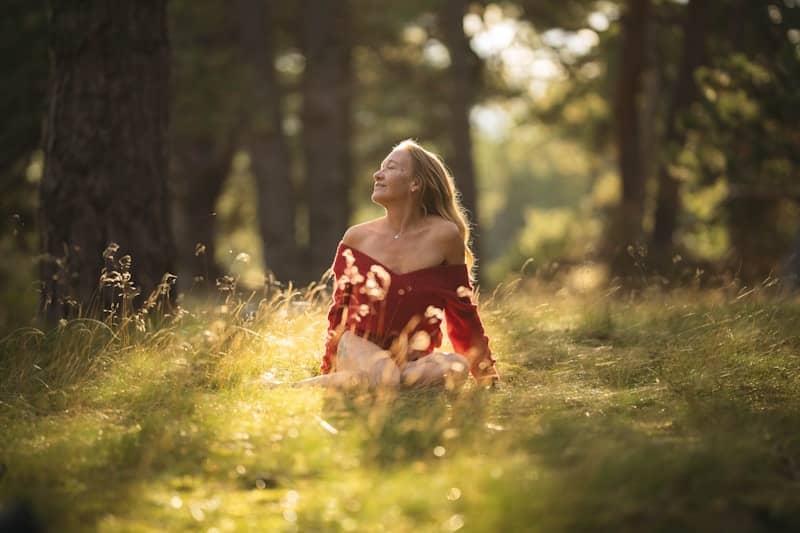 Woman in red top sitting in sunlit grassy forest