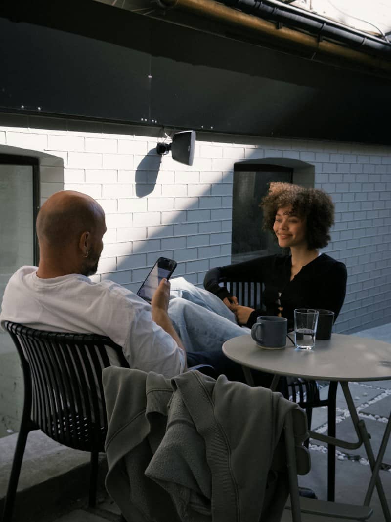 A man and a woman sitting at a small table on a patio in warm light