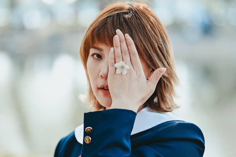 Woman covering eye with hand wearing flower ring