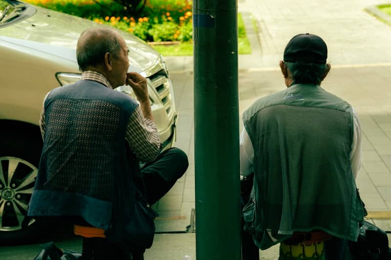 Two elderly men sitting by a car
