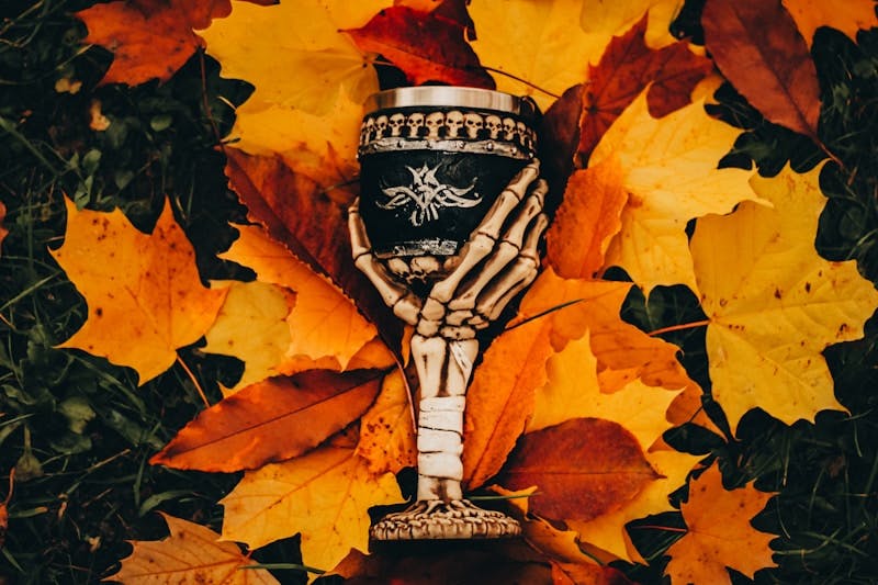 A skeleton hand holding a vase surrounded by autumn leaves