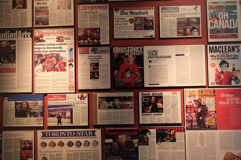 A wall covered in framed newspaper clippings and magazine covers about poutine