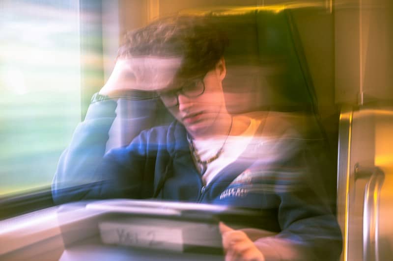 A person with glasses in a blue hoodie sitting on a train