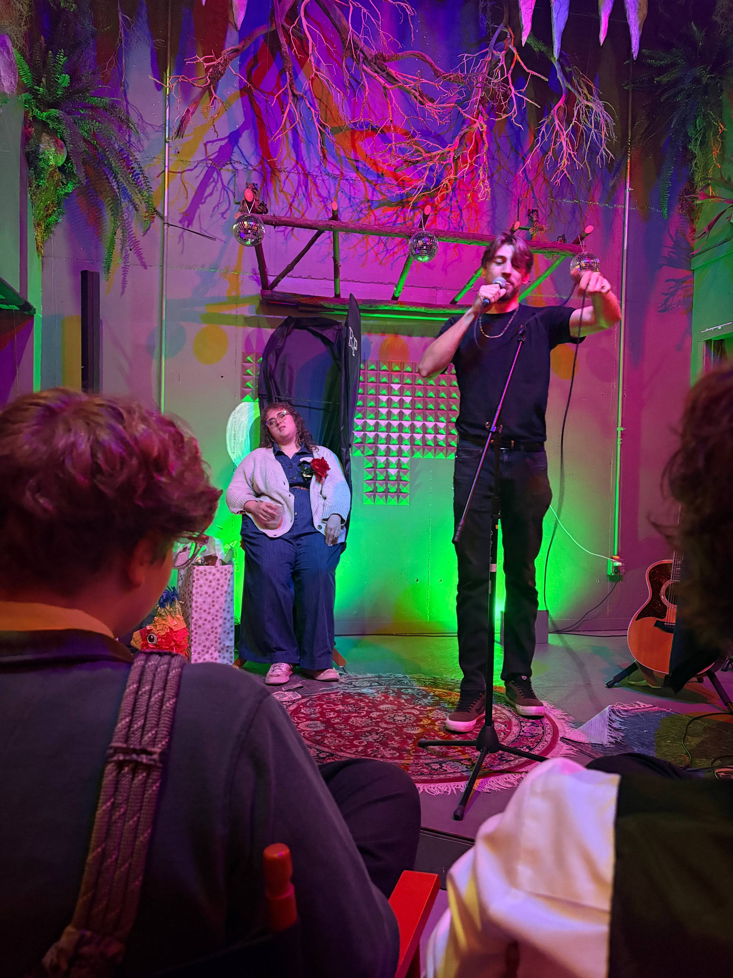 Two people on stage at a mock funeral roast, one at the mic, one in the casket