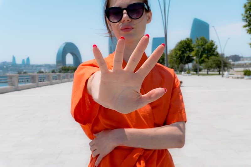 Woman in orange shirt holds up hand outdoors