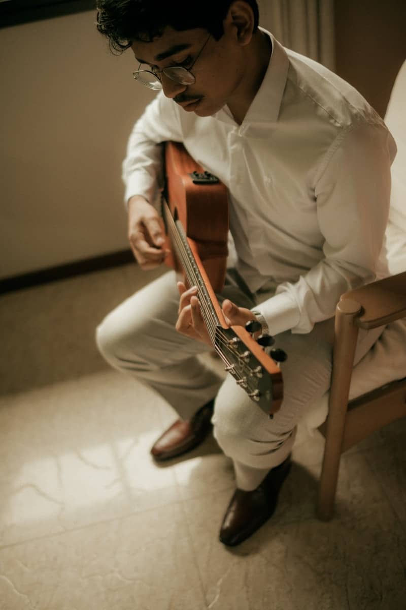 Man in white shirt playing acoustic guitar while seated.