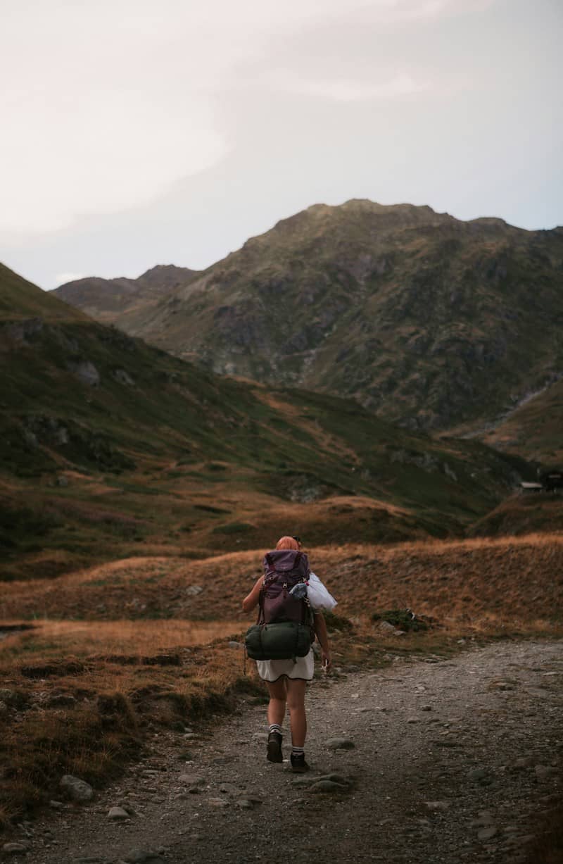 A person with a large backpack walking along a dirt path in mountains
