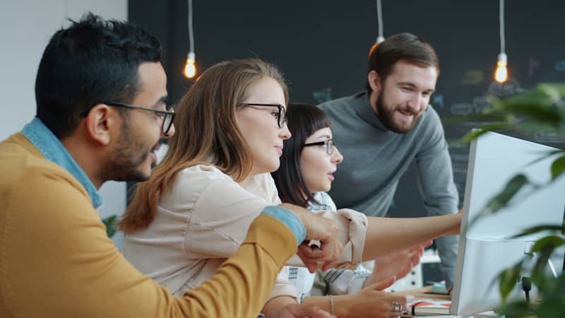 Diverse team collaborating around a computer screen showing the opposite of a lack of commitment