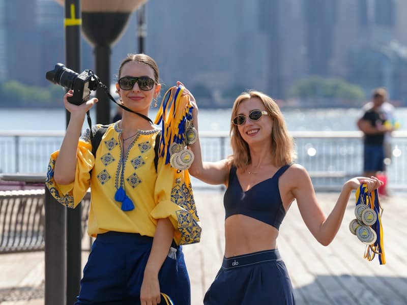 Two women holding medals with blue and yellow ribbons on a wooden pier