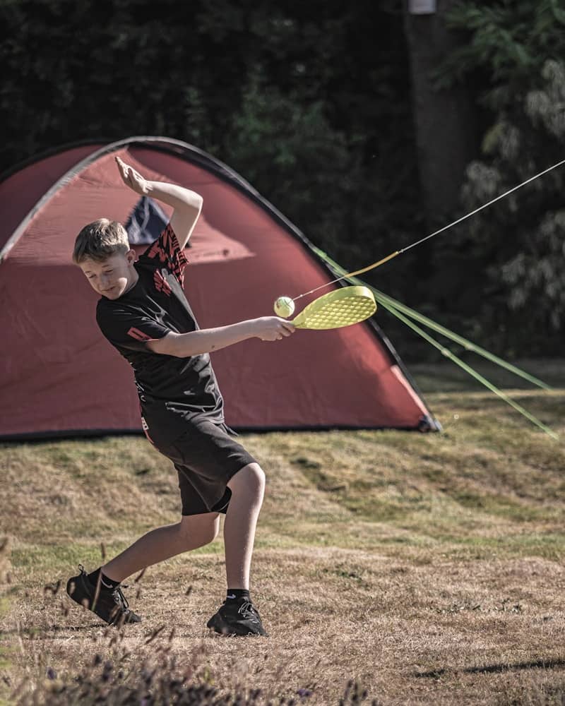 Young boy playing paddle ball near a red tent.