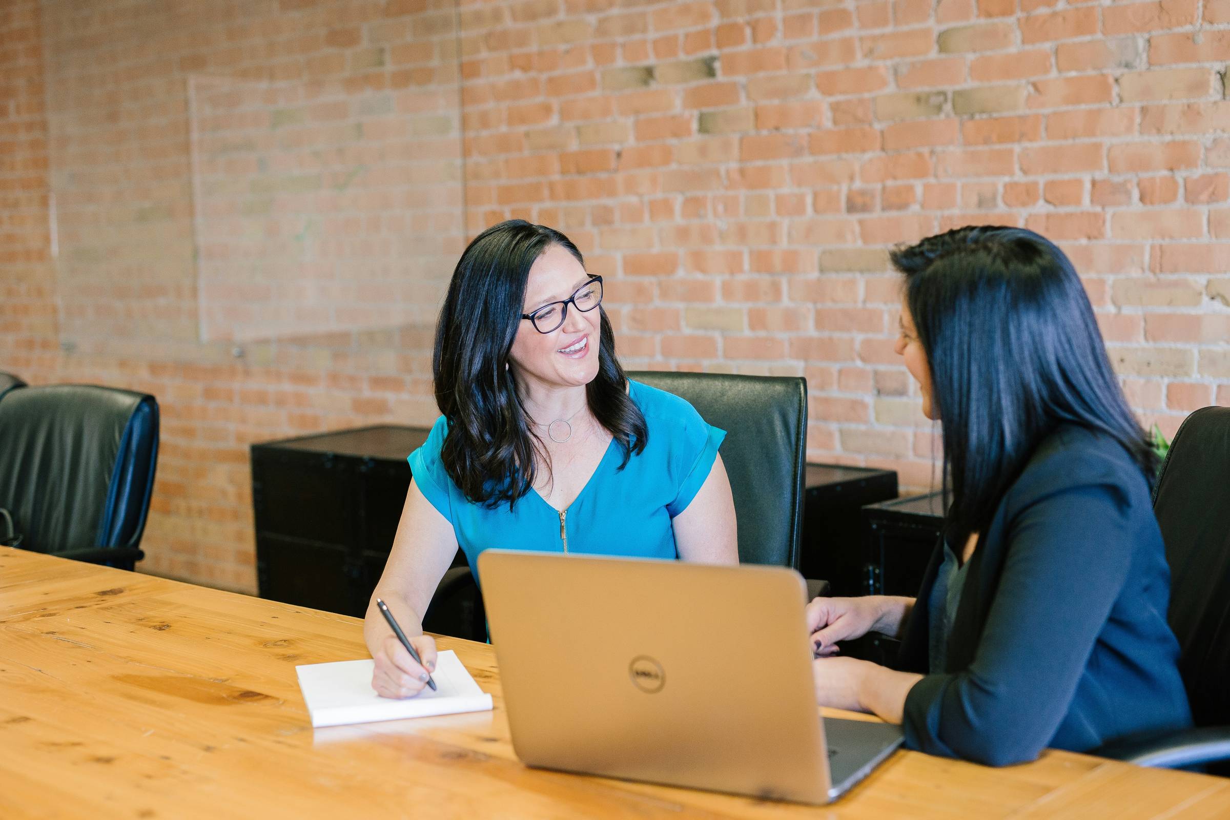 Woman in teal t-shirt sitting next to a woman in a suit jacket.