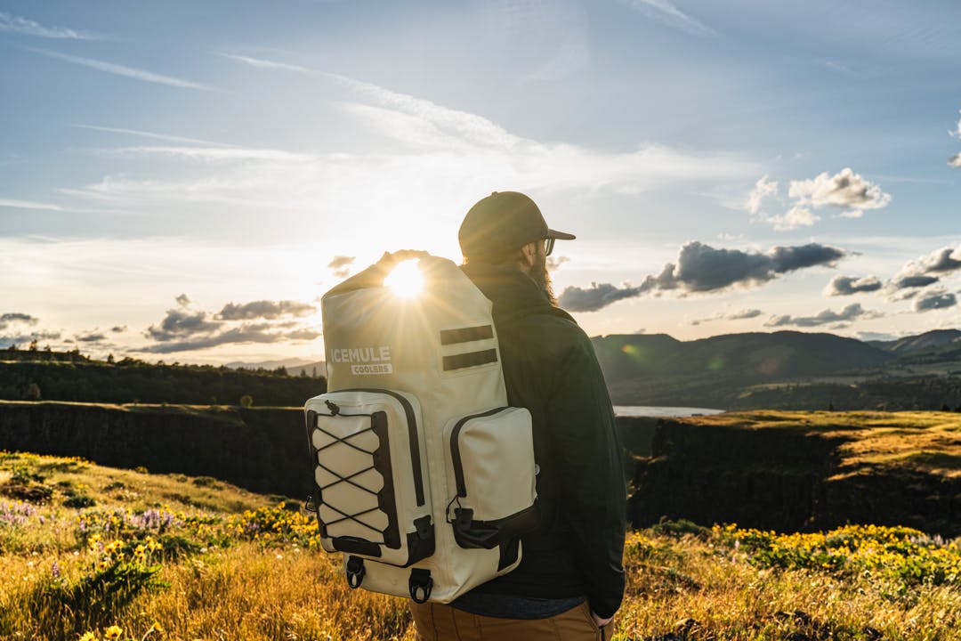 man stands looking out at sunset wearing icemule boss cooler with sunburst shining through closure loop