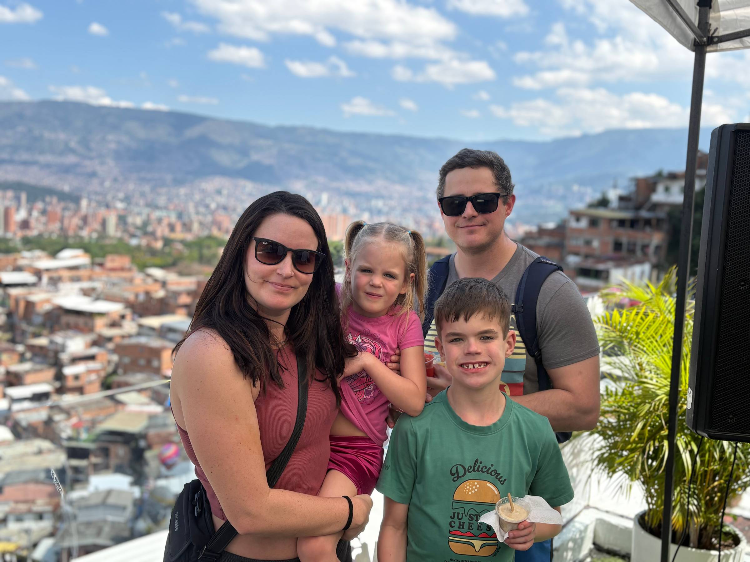 a family smiling for the camera on a peak over the city of medellin, columbia