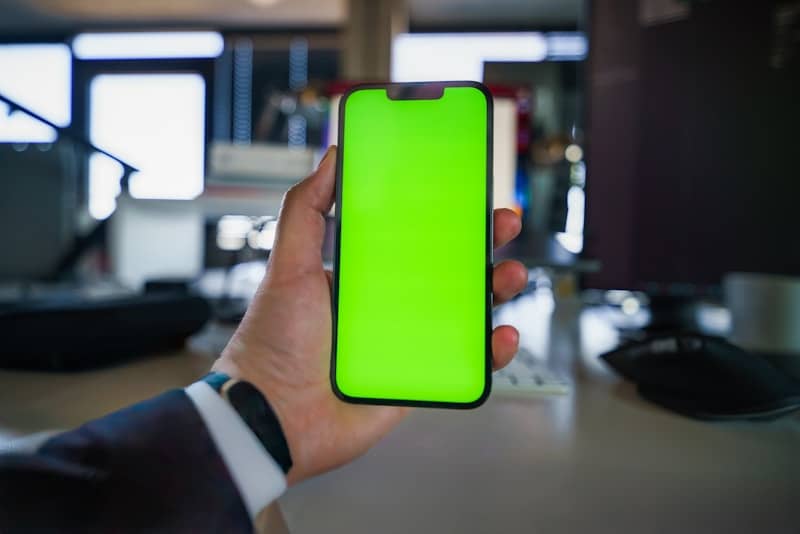 A person holding a cell phone with a green screen