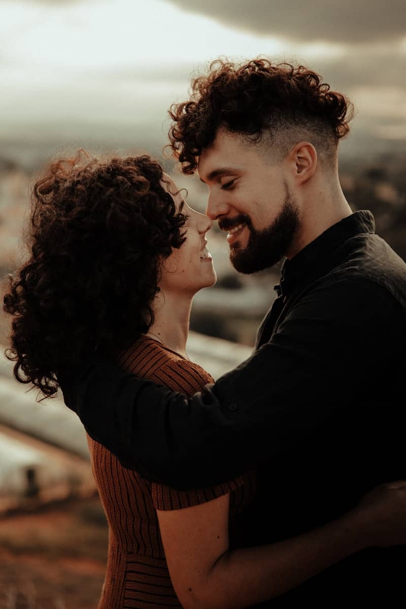 man in black long sleeve shirt kissing woman in orange long sleeve shirt