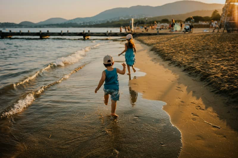 Two children running along the wet sand of a beach at golden hour