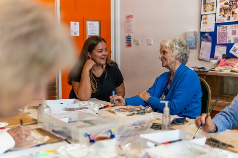 A young woman and an older woman talking at a table during an art class