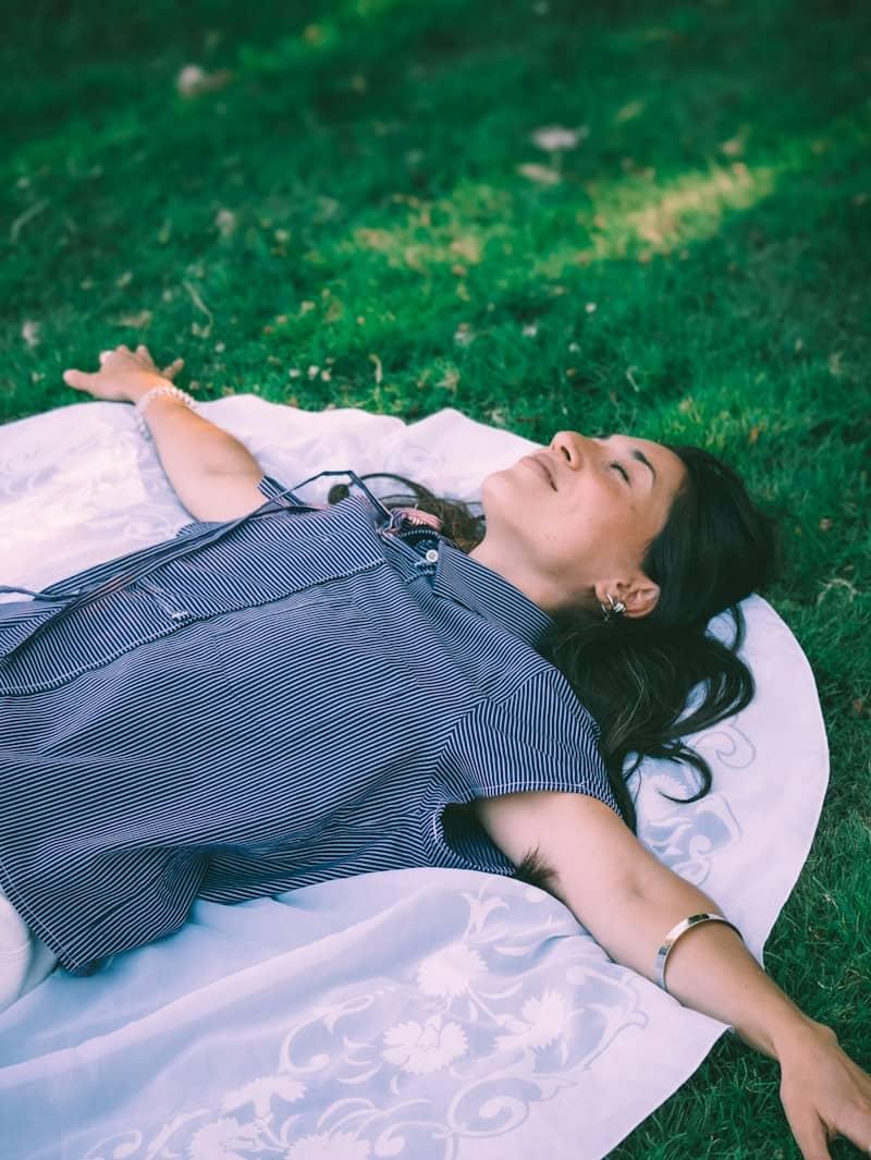 A woman in a striped shirt lying on a white patterned blanket on green grass