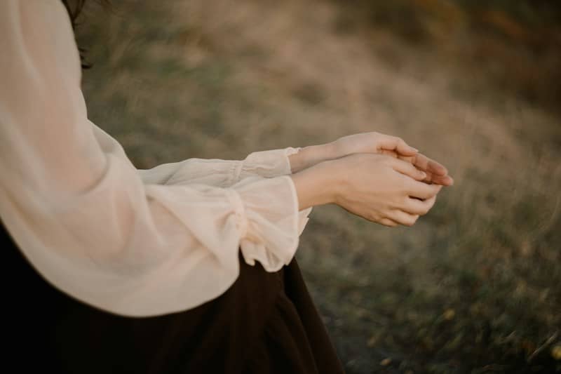 A person with hands cupped together wearing a sheer beige blouse in a field