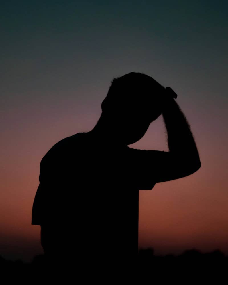 A silhouette of a person with a hand on their head against a gradient sky