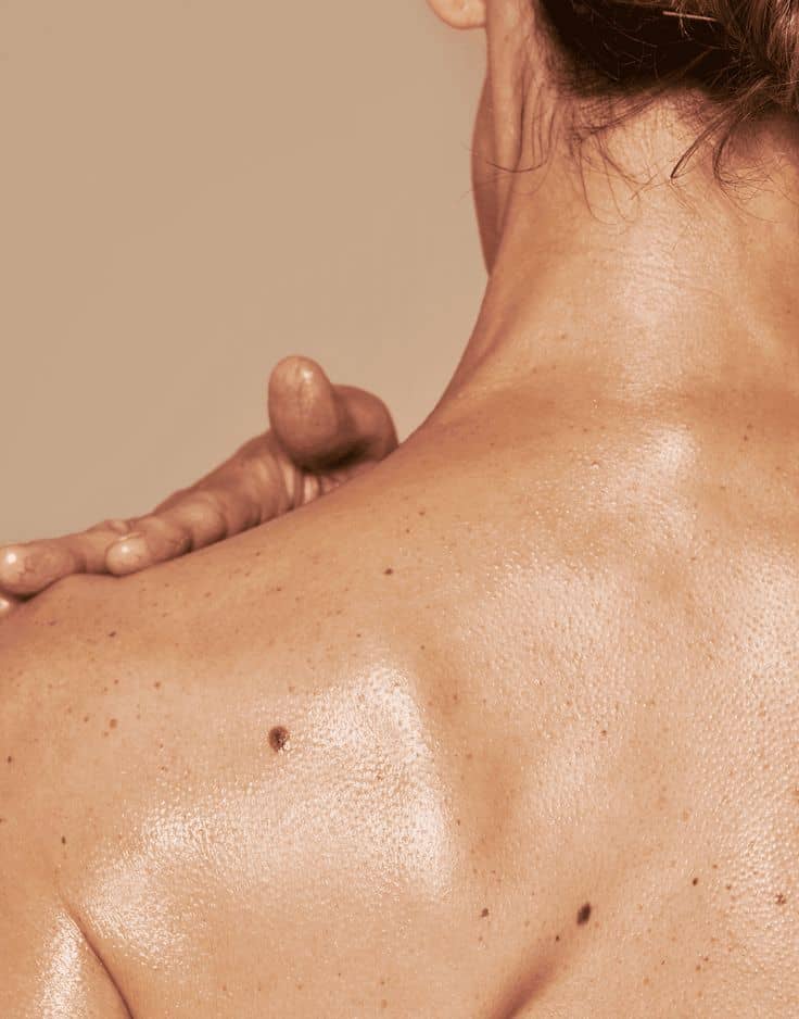 Gros plan d’un dos nu avec une main posée sur l’épaule, peau lisse et lumineuse, concept de soin du corps et bien-être.