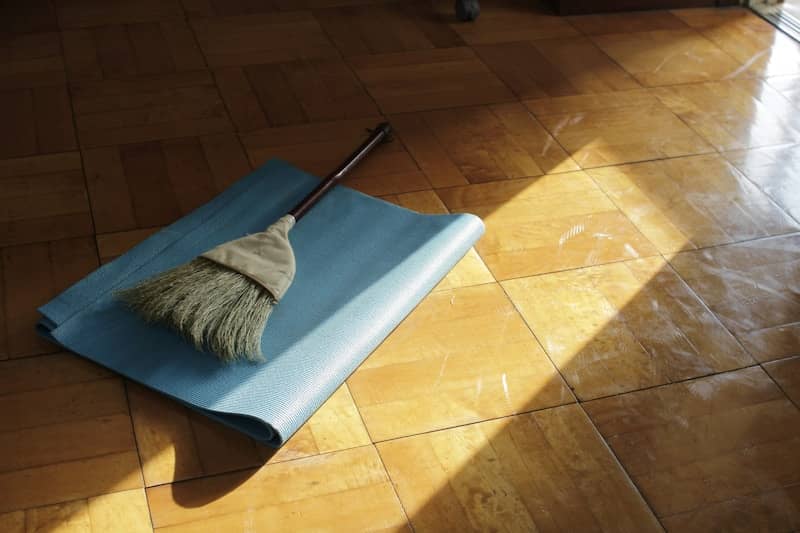 A straw broom resting on a blue yoga mat on a wooden floor