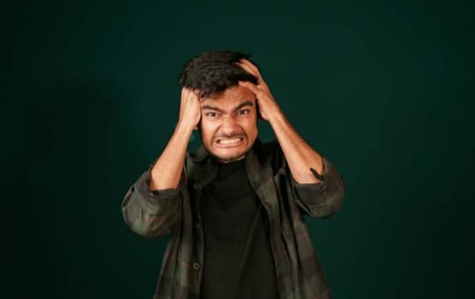 A man in a plaid shirt clutching his head with both hands