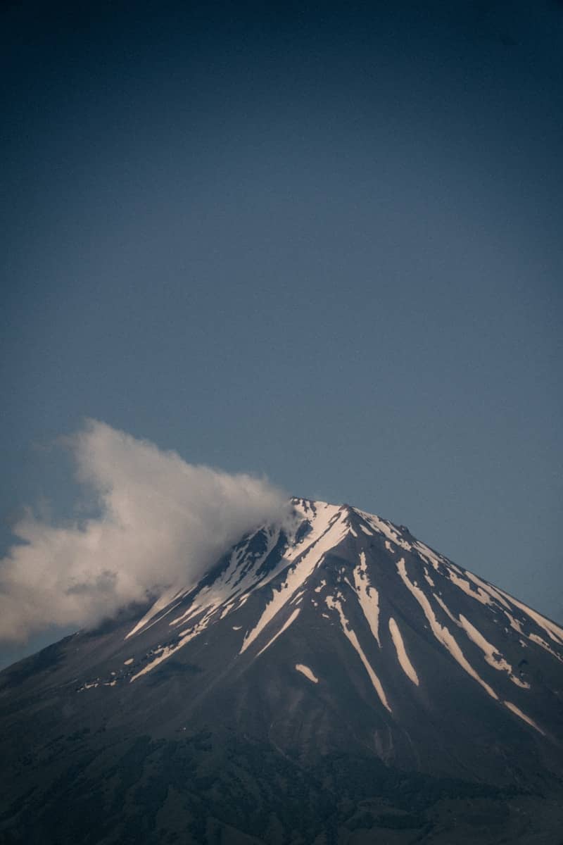 Snow-capped mountain peak with clouds under a clear blue sky.
