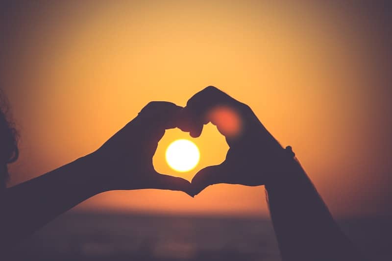hand making a heart over a sunrise