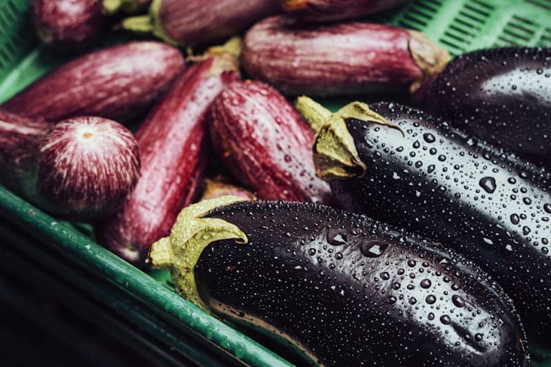 A green basket filled with eggplant and other vegetables