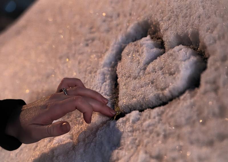 A hand draws a heart shape in the snow.