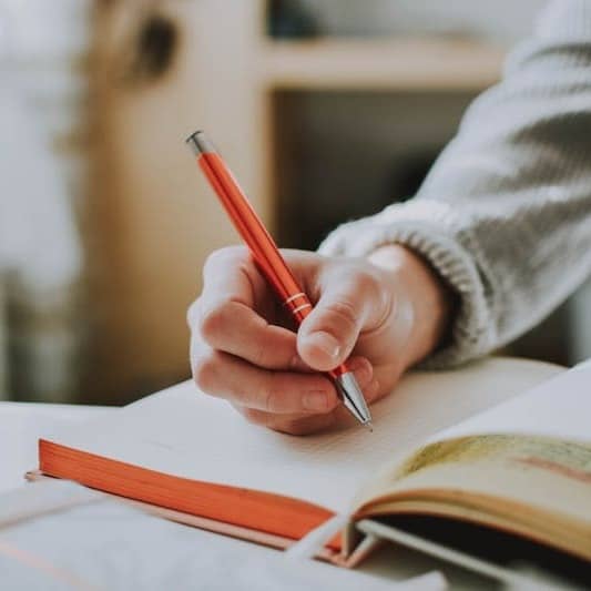person holding on red pen while writing on book