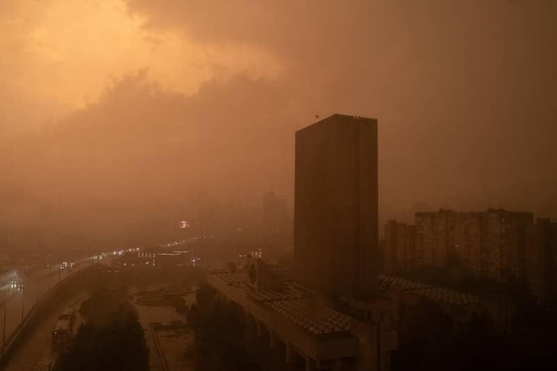 A tall building in Kyiv under a thick, hazy orange sky at dusk.