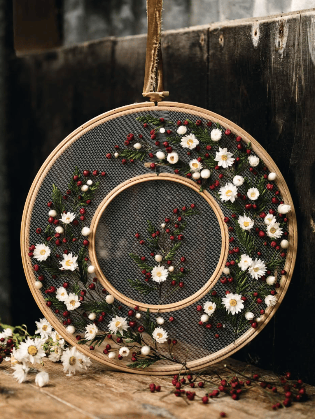 An embroidered ornament made with white dry flowers, evergreen twigs, and small red berries.