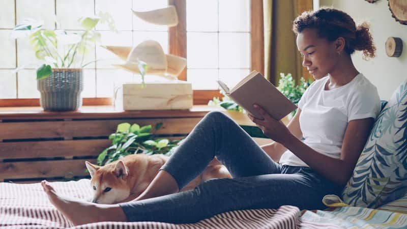 A woman reads a book relaxing with her dog.