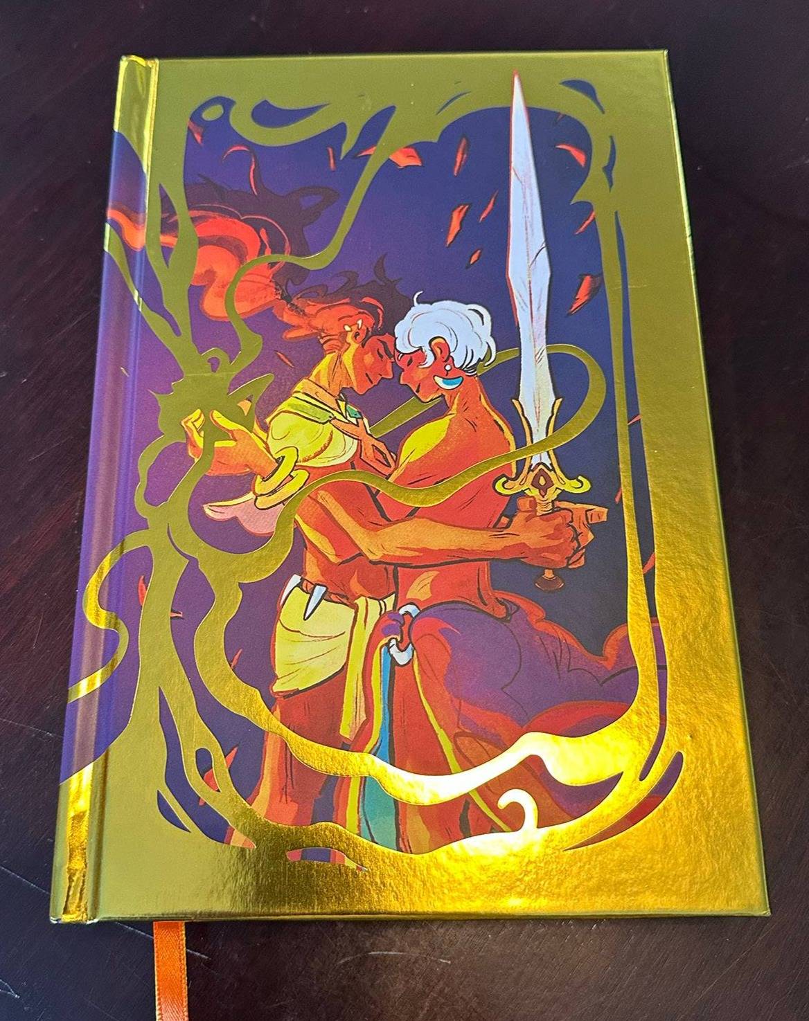 The gold foil-covered special edition of Defy the Gods, with two adventurers embracing