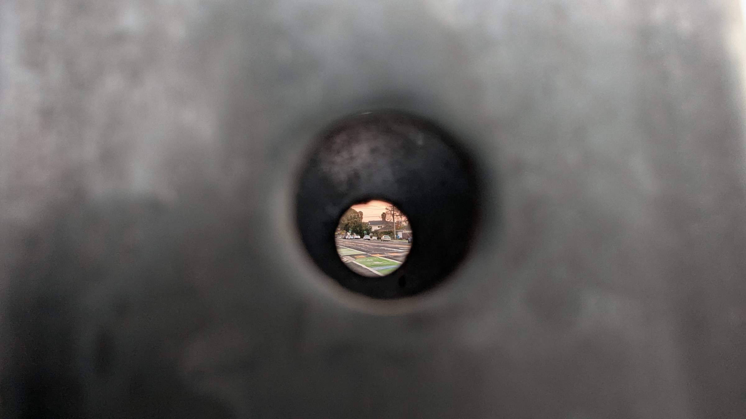 Looking through a hole in a street sign pole to the city street