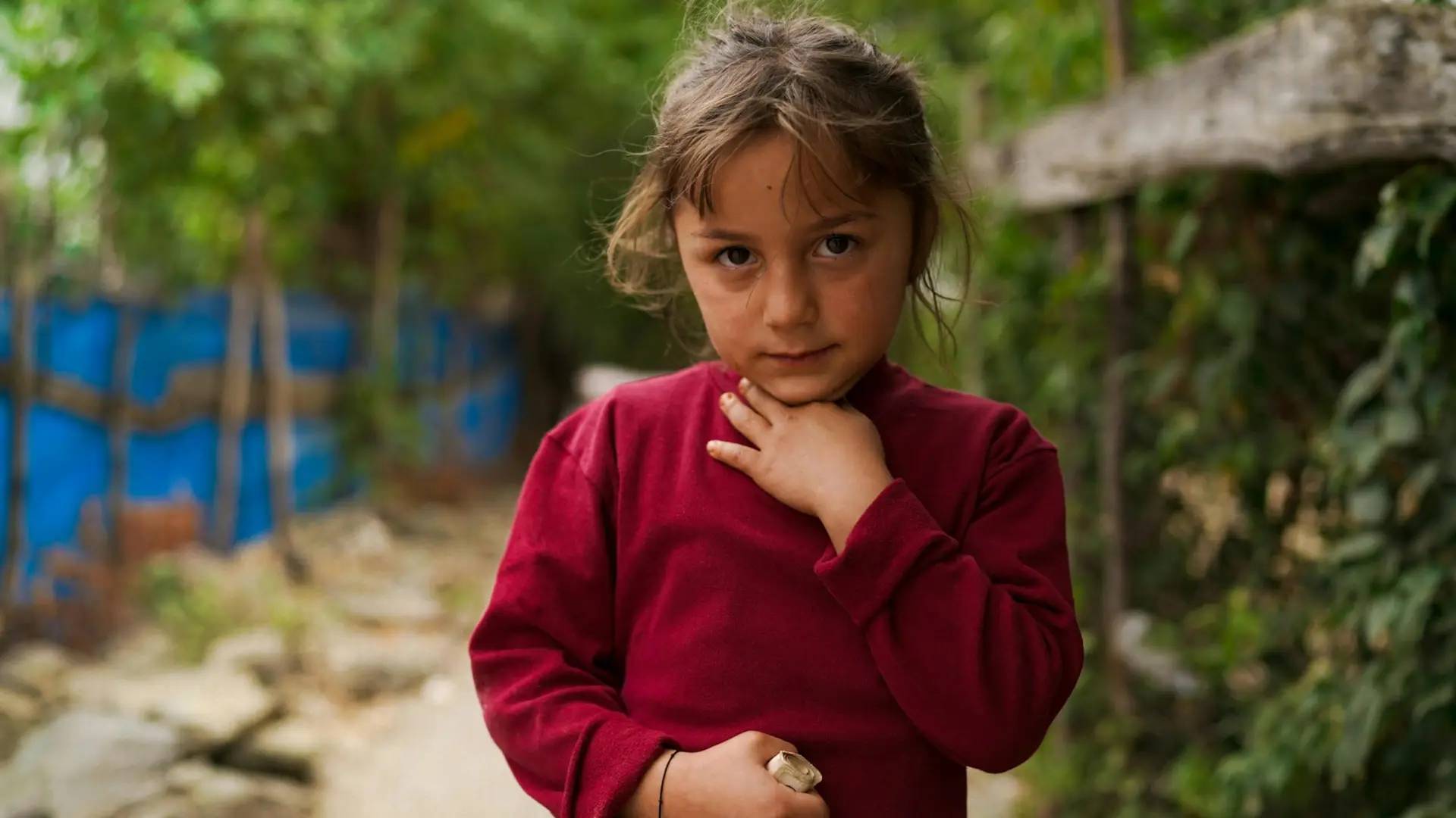 A young girl holding her throat and stomach looking straight to camera