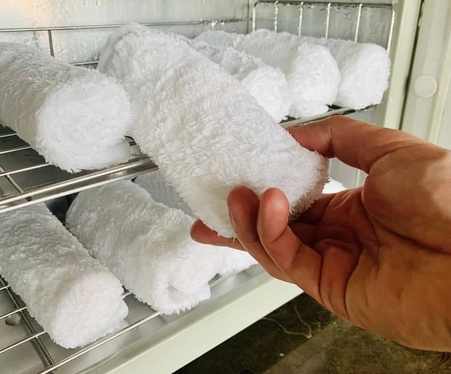 A hand removing a cold white towel from the fridge.