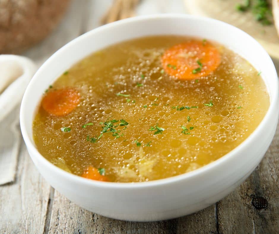 A bowl of vegetable broth with slices of orange carrots in a white bowl.