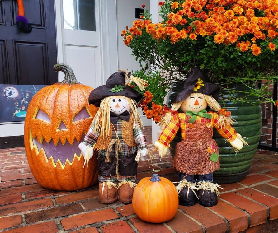 Halloween front door decorations that include orange mums, dolls, and orange pumpkins.
